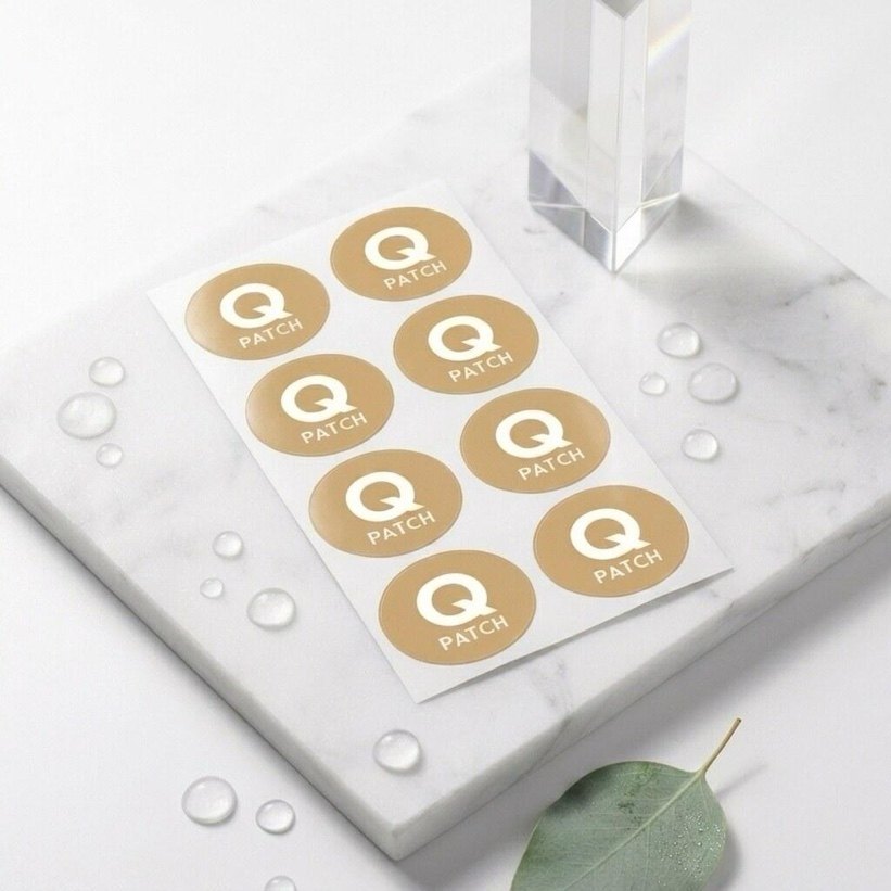 Sheet of QPatch-branded patches on a marble block beside a eucalyptus leaf